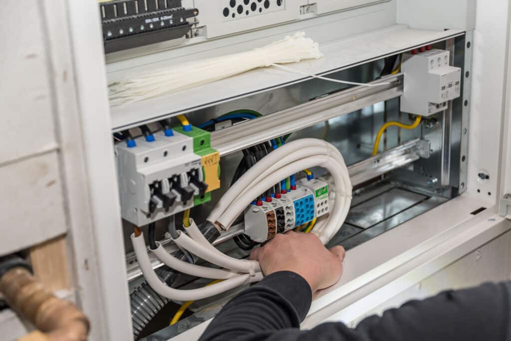 Auf den Bild ist eine Schaltschrank zu sehen und der Monteur hält Kabel in der Hand.